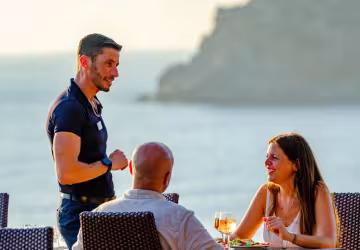 Serveur accueillant un couple attablé face à la mer