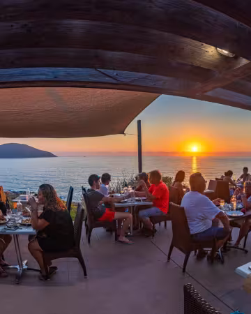 Terrasse du restaurant pleine de convives au coucher du soleil, face à la mer