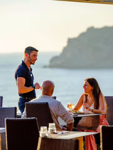 Serveur accueillant un couple attablé face à la mer